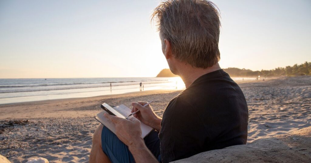 man on the beach using his time to write